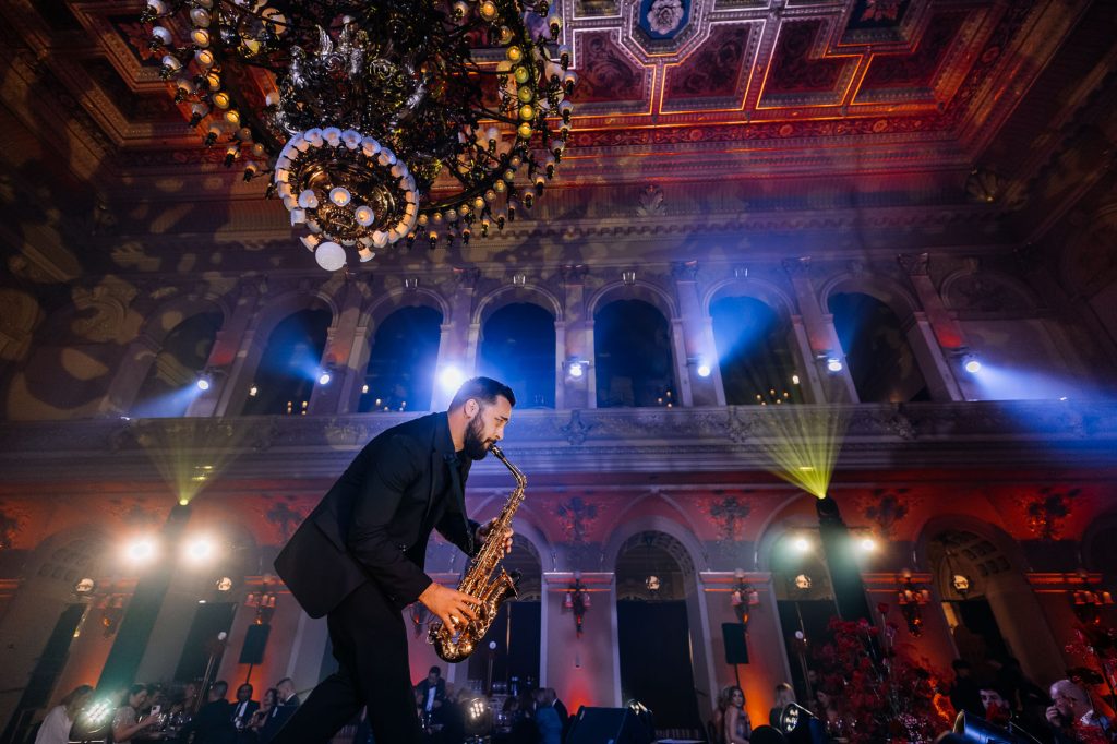 Saxofonista BURYSAX hraje na pódiu v historickém sále s lustry na firemním galavečeru